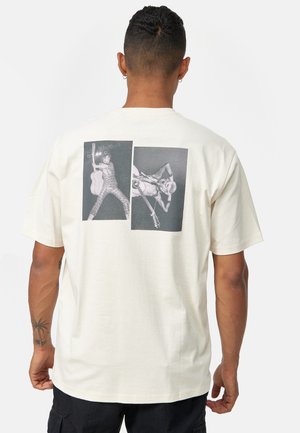 T-shirt crème à manches courtes en coton, avec deux impressions graphiques en noir et blanc au dos représentant des musiciens avec des guitares.