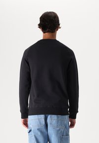 Felpa nera con colletto a girocollo e polsini a coste, con una texture liscia e un design semplice. Indossata con pantaloni cargo blu chiaro.