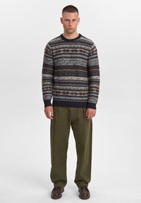 Strikket sweater med flerfarvede vandrette striber i blå, brun og creme. Ribbet halsudskæring og manchetter. Sammen med olivengrønne bukser.
