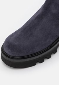 Bout bleu marine en daim avec semelle crantée épaisse noire, avant arrondi et couture visible le long du bord de la semelle.
