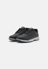 Black golf shoes with smooth leather upper, lace-up design, grey rubber sole, and molded spikes for traction. Minimalist branding on tongue.