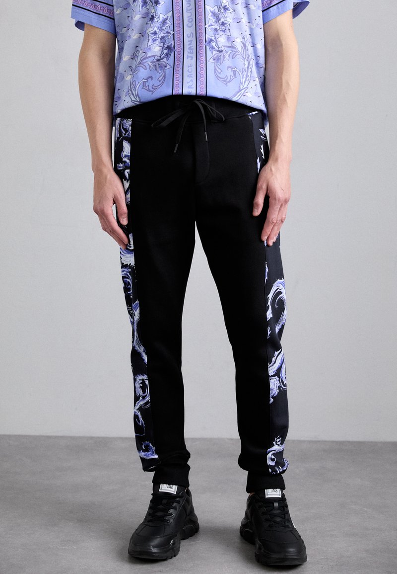 Melni sporta bikses ar sānu paneļiem, kuros ir zilas un baltas vijas formas raksts. Izgatavotas no mīksta auduma ar regulējamu jostu un ietamborētām potītēm.