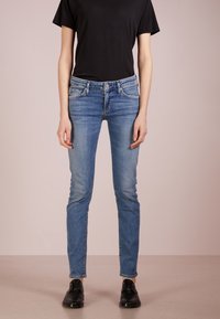 Blå denimjeans med slim fit och medelhög midja, framfickor och subtila blekningar. Matchas med en svart t-shirt och svarta skor.