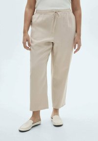 Beige textuurbroek met een elastische taille en verstelbaar koord, met een losse pasvorm en rechte benen, gecombineerd met lichte schoenen.
