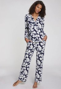 Námornícky modrý pyžamový set s kvetinovým vzorom, ktorý zahŕňa vrchný diel s dlhými rukávmi a gombíkmi a nohavice s elastickým pásom, zdobený bielymi kvetmi a bočnými vreckami.