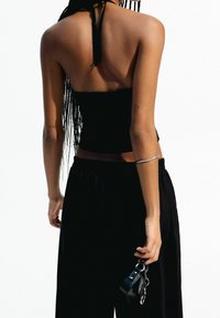 Svart, ärmlös croppad topp med halterneck-design, kombinerad med fladdrande svarta byxor. Inkluderar ett enkelt silverarmband och en liten väska.