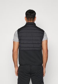 Czarna bezrękawnikowa kamizelka puchowa z prążkowaną teksturą na górnej części, w połączeniu z szarym topem z krótkim rękawem, o prostym wzornictwie.