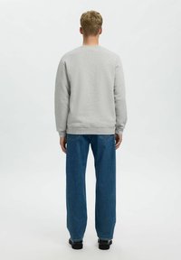 Sweatshirt gris avec un col rond, des manches longues et des poignets côtelés, associé à un jean bleu ample et des chaussures noires.