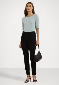 Haut bleu clair à manches longues associé à un jean skinny noir. Sac à main noir tenu à la main, sandales à talons hauts noires. Design simple, accents minimalistes.