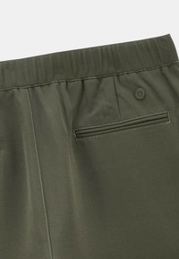 Shorts vert olive avec une taille élastique, dotés d'une poche arrière avec une ouverture horizontale et un détail de bouton décoratif.