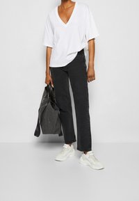 Camiseta blanca de cuello en V, corte relajado, combinada con jeans negros de pierna recta. Tote negra colgada del brazo, y zapatillas blancas con detalles texturizados.