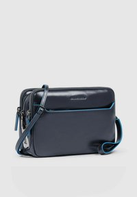 Bolso de cuero azul marino con dos compartimentos con cremallera, acentos azules, correa ajustable y un bolsillo delantero. Textura suave y forma rectangular.