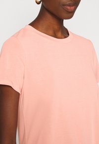 Triko s krátkým rukávem z jemné broskvové látky, s kulatým výstřihem a jemnou strukturou. Jednoduchý, čistý design bez ozdob.