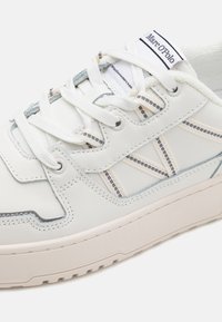 Hvide lædersneakers med grå detaljer. Har teksturerede overlæg, rund tå, snørebåndsdesign og et subtilt logo på tungen.