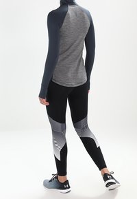 Szary długi rękaw sportowy top z wysokim kołnierzem, w połączeniu z czarnymi legginsami z białym paskowanym wzorem. Szare buty sportowe.