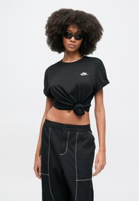 Μαύρο κοντομάνικο μπλουζάκι με δεμένη λεπτομέρεια, με λευκό λογότυπο της Nike. Συνδυάζεται με μαύρο παντελόνι που έχει λευκή ραφή και τσέπες.