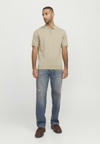 Polo beige à manches courtes avec un col, associé à un jean bleu délavé. La tenue est complétée par des chaussures en cuir marron à lacets.