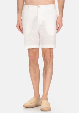 Shorts bianchi in lino con chiusura a un bottone, risvolti e vestibilità rilassata. Abbinati a scarpe beije slip-on, che mostrano uno stile casual.
