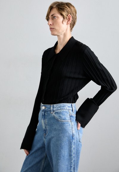 Schwarzes geripptes Langarmshirt mit Kragen und breiten Manschetten, kombiniert mit hellblauen hochtaillierten Jeans. Einfaches Design, strukturierter Stoff.