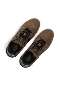 Baskets en suède marron avec des lacets noirs, perforations discrètes et un accent noir texturé. Présentent une semelle en caoutchouc blanche et un détail de logo.