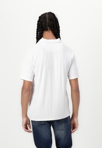Vit kortärmad polo med en strukturerad diamantmönster, med klassisk krage och avslappnad passform, kombinerat med blå jeans.