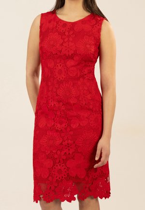 Robe rouge sans manches en dentelle avec motifs floraux, silhouette ajustée et ourlet festonné portée par une femme aux longs cheveux bruns.