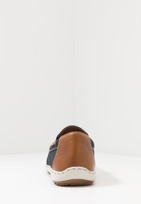 Scarpa slip-on marrone e blu navy con texture perforata, parte posteriore arrotondata e suola di colore chiaro; presenta dettagli cuciti e accenti a contrasto.
