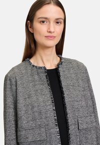 Szary żakiet w jodełkę z postrzępionym kołnierzem i brzegami, z dwoma frontowymi kieszeniami. Noszony na czarną bluzkę, podkreślający zarysowany krój.
