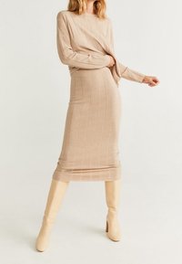 Robe en tricot beige à deux pièces avec des manches longues et une texture côtelée, associée à des bottes beiges jusqu'au genou. Silhouette élégante et ajustée.