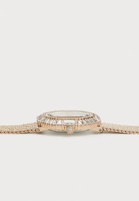 Gold-tone watch featuring an octagonal case with a crystal-accented bezel, mesh bracelet, and clear face with minimal detailing.