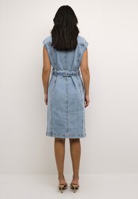 Denim-midi-paita vaaleassa pesussa, jossa on cap-sleeves, vyötäröllä vyö ja jämäkkä muotoilu. Ominaisuuksiin kuuluu polvimittainen helma ja hienovaraiset tikkaus yksityiskohdat.