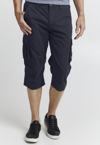 Marinblå cargo shortser med en avslappet passform, knelengde, flere sidelommer og myk bomullsstoff. Kombinert med svarte sneakers.