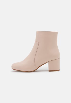 Bottine beige à talon bloc, bout arrondi, finition lisse et détail de couture latérale sur fond blanc.