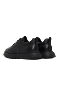 Sneaker in pelle nera con suola spessa, tomaia testurizzata, punta rotonda e design con lacci. Presenta un pratico tirante sul tallone.