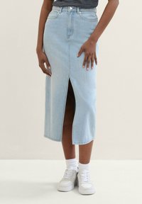 Ljusblå jeanskjol i midilängd med framslits, hög midja och fem fickor. Kombinerad med vita sneakers och vita strumpor som går till ankeln.