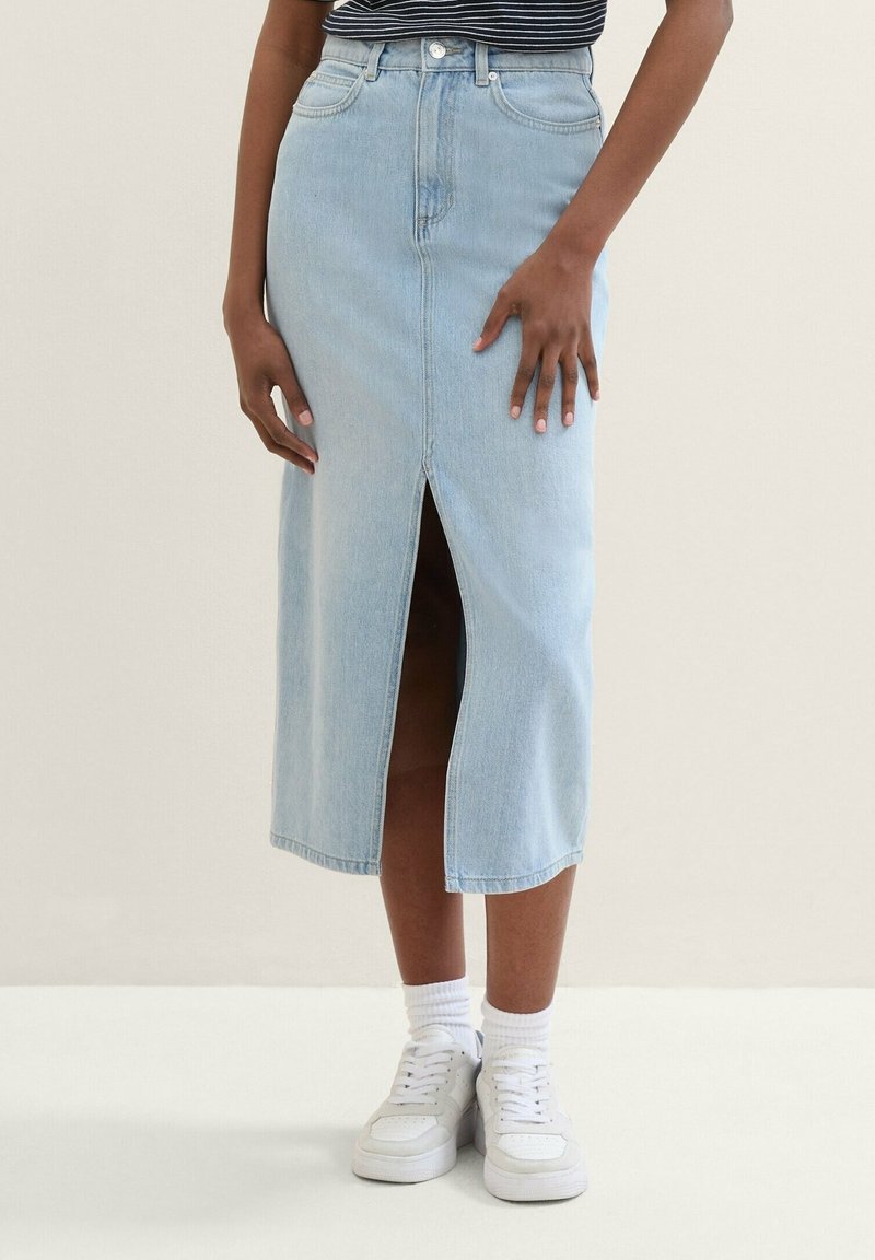 Ljusblå jeanskjol i midilängd med framslits, hög midja och fem fickor. Kombinerad med vita sneakers och vita strumpor som går till ankeln.