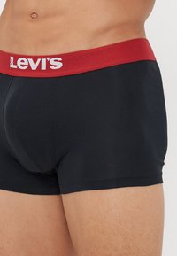 Schwarze Baumwoll-Boxershorts von Levi's mit einem breiten roten Bund, der weißen Logo-Text zeigt. Glatte Textur, enganliegende Passform und minimalistisches Design.