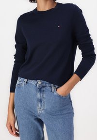 Granatowy sweter z długimi rękawami i okrągłym dekoltem, wykonany z miękkiego materiału, zestawiony z jasnoniebieskimi jeansami o klasycznym kroju z pięcioma kieszeniami.