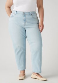 Vaqueros de tiro alto azul claro con un corte relajado, diseño de cinco bolsillos y cierre con botón. Llevados con unos zapatos planos de color crema.