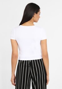 Baltas, liniuotėmis raštuotas, trumpas rankovėmis crop top'as su apvalia iškirpte, kartu derinamas su juodais ir baltais dryžuotais kelnėmis. Paprastas ir prigludęs dizainas.