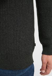 Suéter de punto gris oscuro con puños y dobladillo acanalados, que presenta un patrón texturizado y una pequeña etiqueta en el lateral.