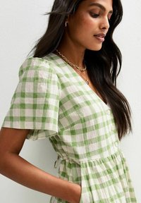 Grün-weiß kariertes Kleid mit kurzen Puffärmeln, V-Ausschnitt, vorderen Knöpfen und geraffter Taille, aus einem leichten, strukturierten Stoff gefertigt.