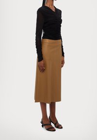 Musta pitkähihaine paita, jossa on rypytettyj�ä yksityiskohtia, yhdistettynä ruskeaan polvipituiseen hameeseen. Mustat naru korkokengät täydentävät asua.