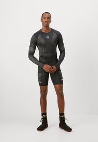 Completo sportivo compressivo nero composto da una maglietta a maniche lunghe con dettagli testurizzati e pantaloni corti, abbinato a calzature nere e gialle.