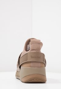 Zapatilla Timberland beige con textura de malla y ante, que cuenta con un talón acolchado, asa trasera y suela de goma texturizada.