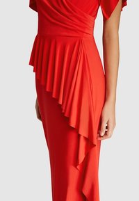 Robe rouge avec des plis sur le côté, en tissu doux, à la coupe ajustée et aux manches courtes drapées. Texture lisse et couleur vive.