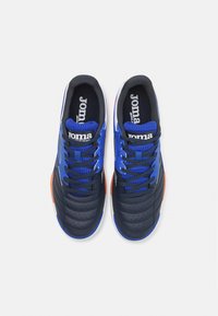 Zapatilla azul y negra con parte superior de cuero perforado, lengua texturizada y cordones oscuros. Presenta acentos naranjas en la suela.