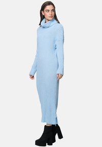 Hellblaues Strickkleid mit einem Schalkragen, geripptem Muster, langen Ärmeln und seitlichen Schlitzes, kombiniert mit schwarzen Plateaustiefeln.