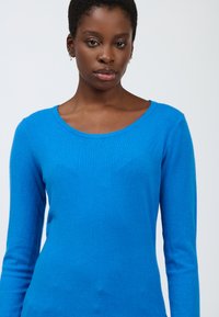 Maglione blu a maniche lunghe realizzato in morbido tessuto a maglia, caratterizzato da un collo rotondo e una silhouette aderente. Texture liscia con dettagli minimi.