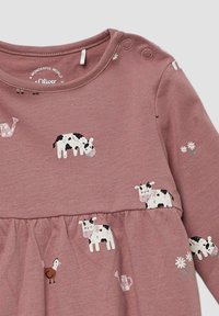 Langsleeve jurk van zachtroze stof met bedrukte zwart-witte koeien, een vogel, bloemen en gieters. Drukknopen aan de schouder.